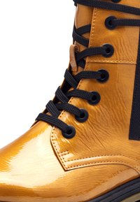 Bottine à lacets en métal doré avec une surface texturée, lacets noirs et œillets ronds ; présente un panneau d'accent noir sur le côté.