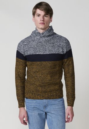 Suéter de punto con cuello de tortuga; presenta rayas en color marino, gris y mostaza. Tejido texturizado con un dobladillo acanalado. Se lleva con jeans de un color azul claro.