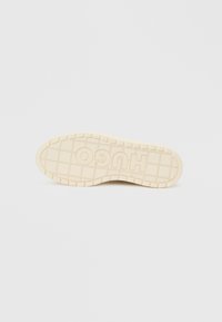 Beige rubber shoe sole with a textured grid pattern and raised "HUGO" logo. Outline features a curved shape for enhanced grip and flexibility.