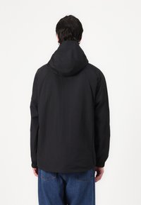 Black hooded jacket with a smooth texture, elastic cuffs, and a straight cut. Worn with loose-fitting blue jeans.