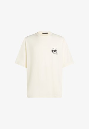 T-shirt couleur crème avec une coupe ample, des manches courtes, un col rond et un graphique d'une personne portant des lunettes de soleil sur la poitrine gauche.