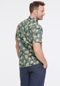 Camicia a maniche corte, con colletto, di colore verde con un motivo floreale che presenta fiori arancioni, bianchi e blu, realizzata in tessuto leggero.