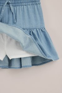 Blauer Jeansrock mit elastischem Bund, gebundener Kordel, gerafftem Saum und weißem Innenfutter-Detail.