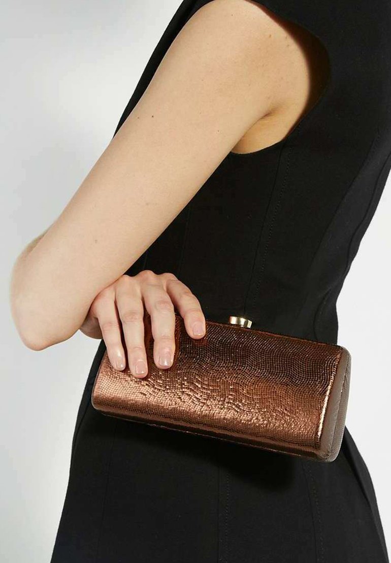 Metallic bronze clutch purse with a textured finish, rectangular shape, and a gold clasp, held in a hand against a black garment.