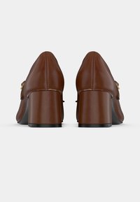 Chaussures à talons en cuir marron avec un bout rond, ornées d'une petite boucle décorative et d'un talon épais noir. Texture lisse.