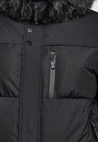 Czarna kurtka puchowa z kołnierzem z futerka ekologicznego, kieszeniami na zamek oraz połączeniem gładkich i fakturowanych paneli materiału.