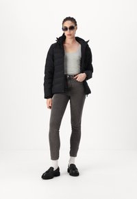 Chaqueta de plumas negra, top gris ajustado, jeans skinny gris oscuro, zapatos gruesos negros y gafas de sol; texturas suaves y diseño moderno.