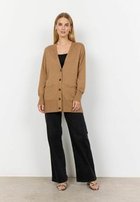 Bruine gebreide cardigan met een V-hals, knoopsluiting aan de voorkant, geribde manchetten en twee voorzakken, gecombineerd met zwarte wijde broek.