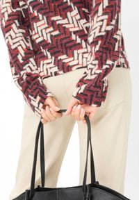 Maglione a maglia multicolore con motivo a zigzag in bordeaux, crema e grigio, abbinato a pantaloni beige chiaro e una borsa in pelle nera.