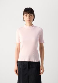Helles rosa, geripptes T-Shirt mit kurzen Ärmeln, hohem, fransigem Kragen und dekorativen Hardware-Details. Glatte Textur und taillierter Schnitt.