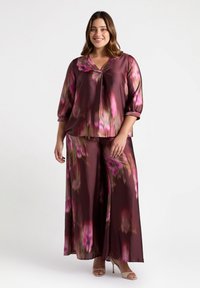 Completo due pezzi fluido in satin bordeaux con motivi floreali rosa. Caratterizzato da scollatura a V, maniche a tre quarti e pantaloni a gamba larga.