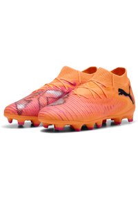 Scarpe da calcio arancioni con tomaia texturizzata, caratterizzate da un logo nero e accenti rosa sulla suola. Design leggero e aerodinamico per prestazioni elevate.