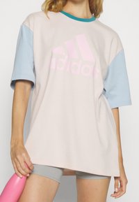 Rosa och ljusblå oversized t-shirt gjord av mjuk bomull, med en stor rosa Adidas-logotyp på framsidan och korta ärmar.