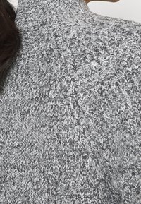 Stickad turtlenecktröja i grått med ett texturerat, ribbat mönster. Tyget ser mjukt och tjockt ut med varierande nyanser av grått.