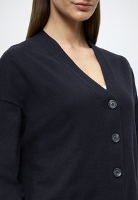 Cardigã de malha azul marinho escuro com decote em V, apresentando quatro botões na frente e uma textura suave.