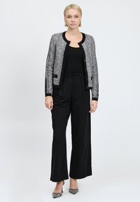Cardigan a righe bianche e nere con colletto rotondo, pantaloni neri e décolleté a fantasia bianco e nero. Texture liscia, vestibilità su misura.