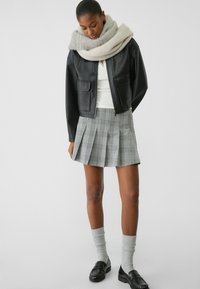 Giubbotto in pelle nera corto, top bianco, gonna a pieghe grigia a quadri, calze a maglia grigia a fantasia e mocassini neri.
