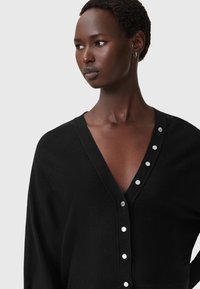 Zwarte cardigan met een diepe V-hals, voorzien van metalen knoopaccenten aan de voorkant. Zachte textuur en een ontspannen pasvorm.