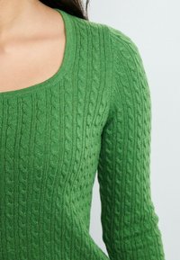Maglione verde lavorato a maglia con scollatura a barca, caratterizzato da un motivo a trecce in rilievo e maniche lunghe, realizzato in un morbido materiale testurizzato.