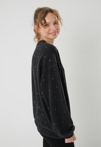 Felpa nera oversize realizzata in morbido tessuto, decorata con macchie argento diffuse. Presenta spalle scese e polsini a coste.