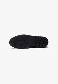 Black rubber shoe sole with deep, triangular tread pattern and smooth surface. Features a rounded toe and slight curvature at edges.