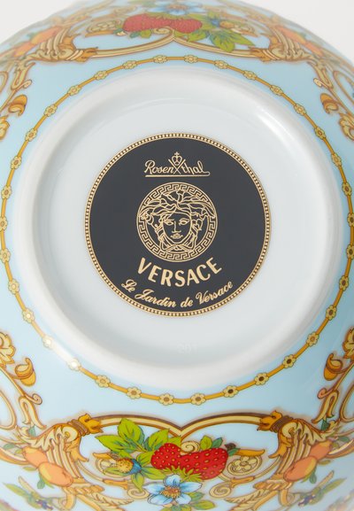 Keramická miska s jemne modrým pozadím, kvetinovými a ovocnými vzormi v živých farbách, so zlatými akcentmi a čiernym logom na spodku.