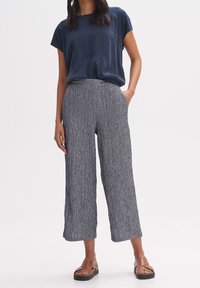 Marinblå kortärmad topp i kombination med vida byxor som har ett strukturerat marinblått och vitt mönster. Bruna sandaler kompletterar outfiten.