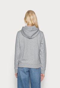 Sweat à capuche gris avec un cordon de serrage, texture douce et poignets côtelés. Associé à un jean large bleu clair, mettant en avant un look décontracté.