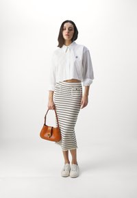 Camisa blanca cortada con botones y un pequeño logo, falda de punto a rayas, bolso beige y zapatillas blancas. Detalles de tela texturizada visibles.