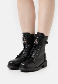 Schwarze Leder-Stiefeletten mit Schnürung, silbernen Hardware-Akzenten, seitlichem Reißverschluss und robuster Sohle. Mit einem Riemen mit dekorativem Detail.