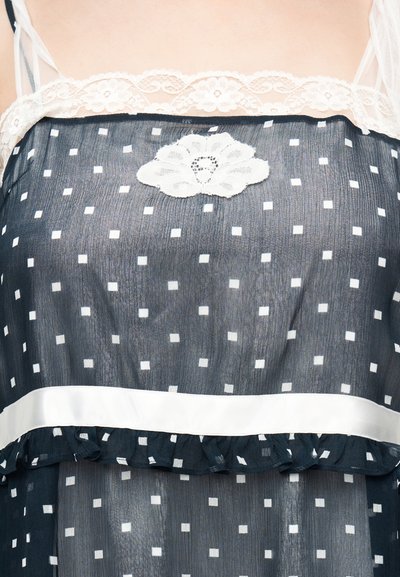 Tissu transparent foncé avec motif de carrés blancs, bordure en dentelle au niveau de l'encolure, application florale en dentelle au centre, et ceinture blanche avec un volant en dessous.