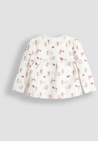 Katoenen top met lange mouwen, voorzien van een witte achtergrond met roze en paarse bloemen- en feeënpatronen. Uitlopende snit met een ronde halslijn.