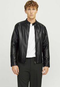 Jachetă din piele neagră cu guler înălțat, buzunare cu fermoar și detalii matlasate pe umeri. Textură netedă și design ajustat. Asortată cu un tricou alb.