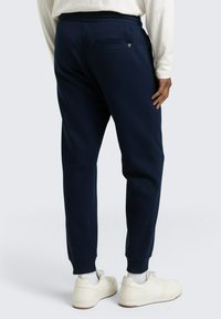 Granatowe dresy wykonane z miękkiego materiału, z tylną kieszenią, elastyczną talią i prążkowanymi ściągaczami. Noszone z białymi trampkami.