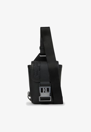 Czarna torba na ramię z gładkiej skóry, regulowanym paskiem, wygrawerowanym logo i metalowymi elementami do zamknięcia.