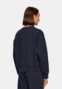 Felpa blu navy con motivo logo in rilievo, scollo a girocollo e vestibilità rilassata con polsini e orlo a coste. Tessuto morbido e testurizzato.