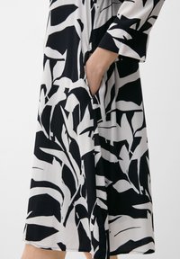 Schwarz-weiße Kleid mit einem auffälligen Blattmuster, langen Ärmeln und einer Seitentasche, aus leichtem Stoff mit einer weichen Textur.