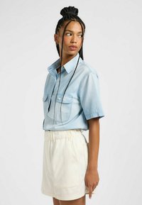 Camisa de botones de manga corta color azul claro con dos bolsillos en el pecho, combinada con shorts de cintura elástica color crema que cuentan con bolsillos laterales.