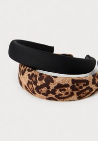 Dva hairbanda: en glad črn trak in en bež trak z rjavim leopardjim vzorcem. Oba sta okrogla in pokrita s tkanino.