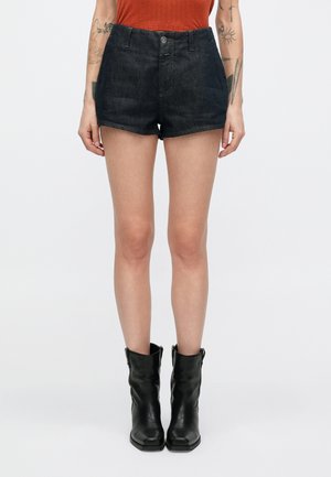Dunkle Jeans-Shorts mit tailliertem Bund, vorderer Knopfleiste und einem sauberen Saumabschluss. Kombiniert mit schwarzen Leder-Stiefeletten.