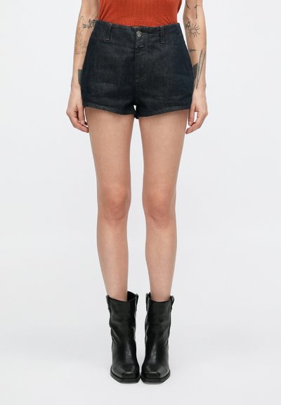 Shorts en denim foncé avec une taille ajustée, une fermeture à bouton sur le devant et une coupe nette à l'ourlet. Portés avec des bottines en cuir noir.