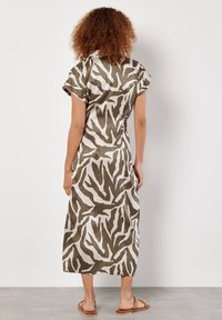 Khakifarbenes und cremefarbenes gemustertes Kleid mit kurzen Ärmeln, Tierdruckdesign, knielange Länge, glatte Textur, kombiniert mit flachen Sandalen.