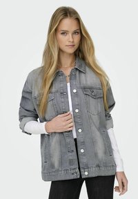 Giacca in denim grigia con chiusura a bottoni, tasche sul petto e vestibilità rilassata. Presenta dettagli usurati e maniche arrotolate.