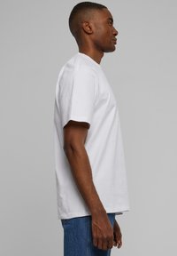 White cotton t-shirt with short sleeves, crew neck design, relaxed fit, shown from the side, paired with blue denim jeans.