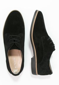 Scarpe nere in suede con punta arrotondata, lacci e suola piatta in gomma testurizzata. L'interno presenta una leggera fodera. Accenti minimali.
