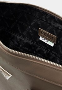 Brown synthetic purse interior with a black fabric lining featuring a repeating "GUESS" logo. Includes a "GUESS ECO" label. Zippered closure.