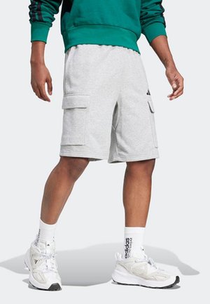 Person trägt graue Cargo-Shorts, weiße Adidas-Socken und weiße Sneaker, mit grünem Sweatshirt sichtbar am Bund.