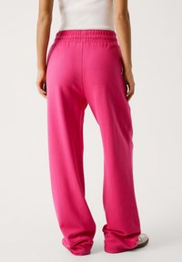 Træk-på, brede sweatpants i lys pink, med elastisk talje og glat tekstur, og løs pasform omkring anklerne.