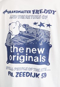 Hvit T-skjorte med blå grafikktrykk. Teksten inkluderer "The Grandmaster Freddy," "the new originals," og "Fri. Zeedijk 59." Den har stjerner og en karakter.