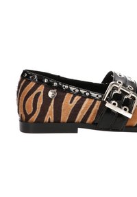 Zapato plano tipo slip-on con tela de print de cebra, acentos de charol negro, una hebilla plateada y detalles de tachuelas a lo largo del borde superior.